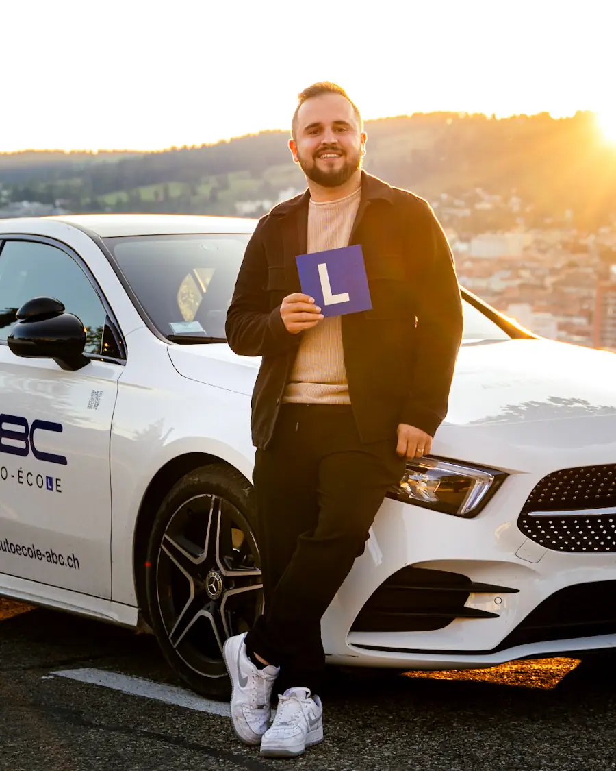 Blerim Ramsha, moniteur de l'Auto-école ABC, le panneau L à la main devant la voiture-école